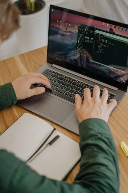 Hands typing on a laptop in close-up beside a cup of coffee on a wooden desk.